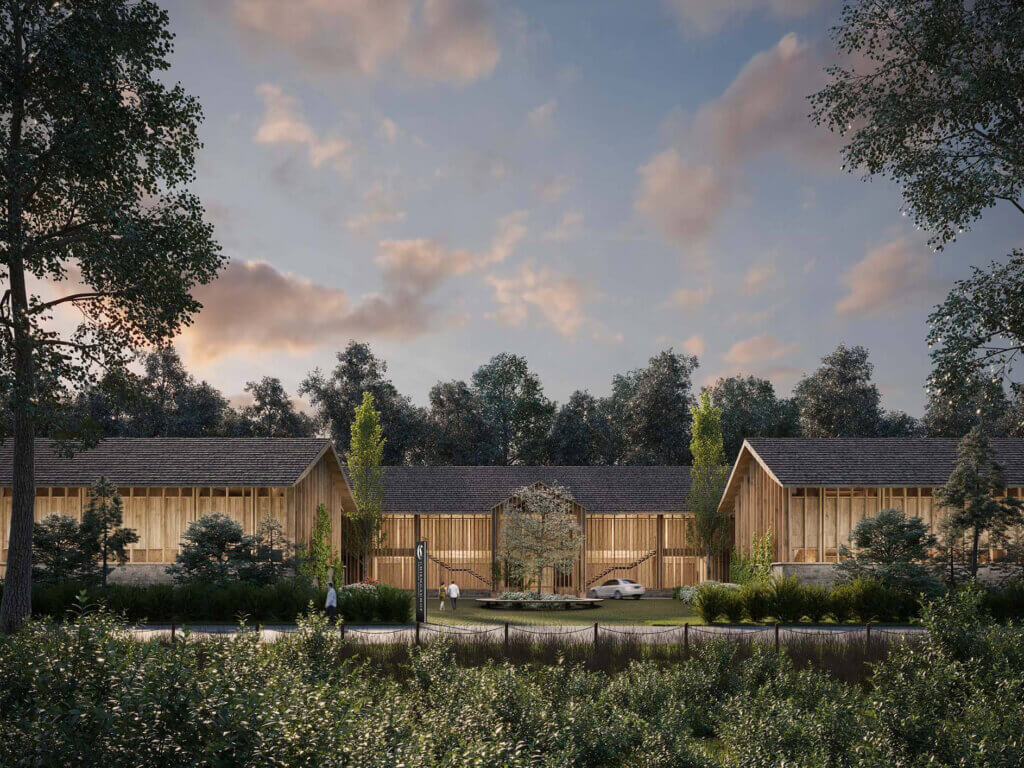 A modern one-story building with a wooden exterior and large windows is surrounded by trees and greenery at dusk. A car is parked in front and a few people are walking along the pathway.