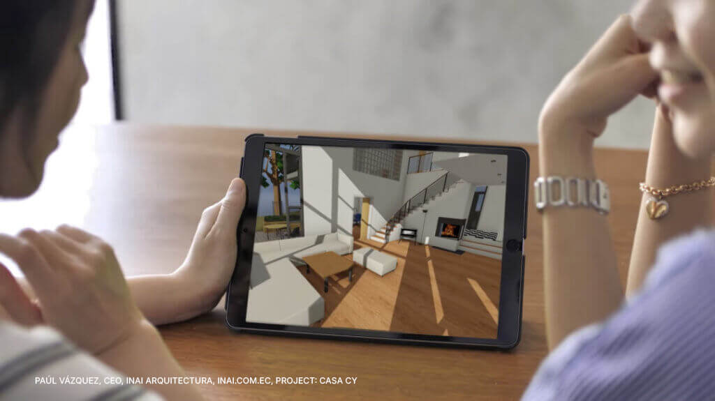 Two people sit at a table, viewing a tablet displaying a 3D architectural rendering of a modern living room with a staircase and large windows.