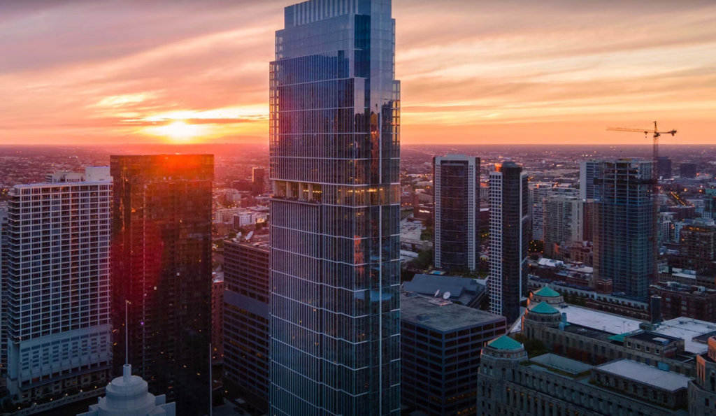 Aerial view of a modern observatory with a domed roof and glass walls, surrounded by parked cars, fields, and a road. The building has a green rooftop and pathways circling it.